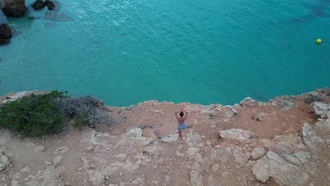 Lovely-aerial-top-view-flight-Yoga-Girl-position-tree-sunset-cliff-beach-island-ibiza-Spain-drone-shot-footage-from-above