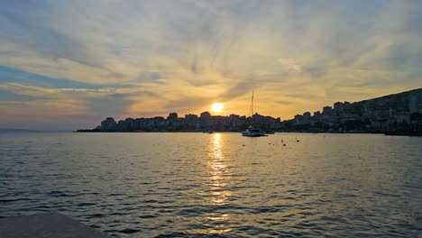 Magischer-Sonnenuntergang-Der-Küstenstadt-Saranda,-Hafen-Und-Bucht,-Glitzerndes-Meer,-Himmel-Mit-Lebhaften-Wolken-Bemalt-–-Eine-Spektakuläre-Abendszene