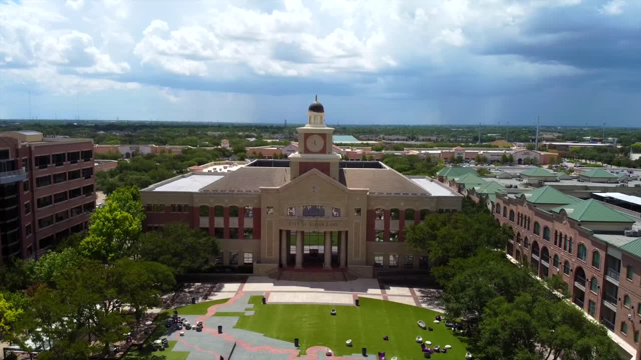 An aerial shot of Sugar Land's Towne Hall Building, on a partly cloudy day, at 60 frames