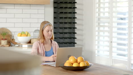 working from home, woman using laptop and writing notes in kitchen