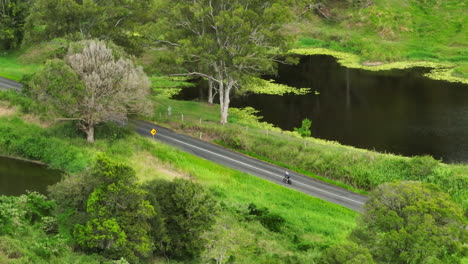 Athlete-Cyclist-Riding-Bike-Along-Scenic-Countryside-Rural-Road-In-Australia,-4K-Drone-Telephoto-Slow-Motion