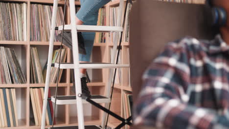 woman ascending stepladder near bookcase. librarian uses foldable set of stairs to access books on upper shelf in library. work of library employee