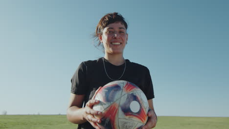 joyous female athlete holding soccer ball and smiling on camera