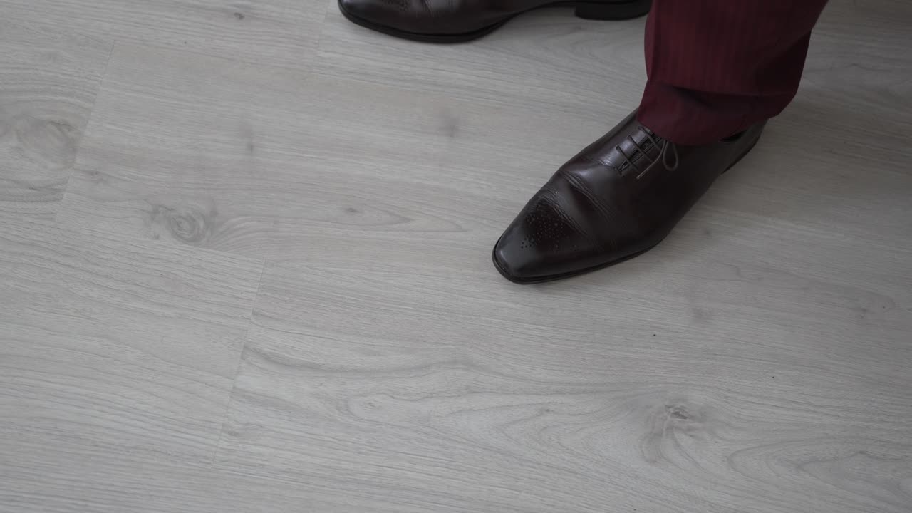 Close up of brown leather dress shoes paired with burgundy pants on light wooden floor