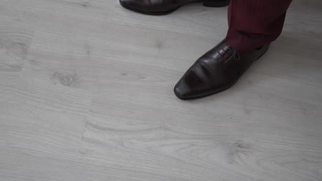 close up of brown leather dress shoes paired with burgundy pants on light wooden floor