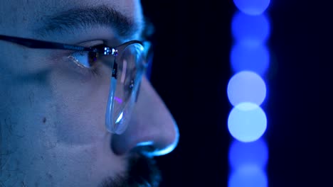 macro shot of the eyes of a young man with galsses live streaming for internet, with gamer style led lights on the background