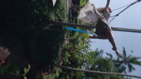 vertical fpv rotating slowmotion shot of a beautiful blond woman spreading her arms and enjoying the swing set in the tropical nature of bali