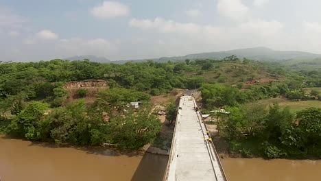 Drone-shot-of-construction-workers-building-a-bridge-over-a-murky-brown-river-in-the-countryside