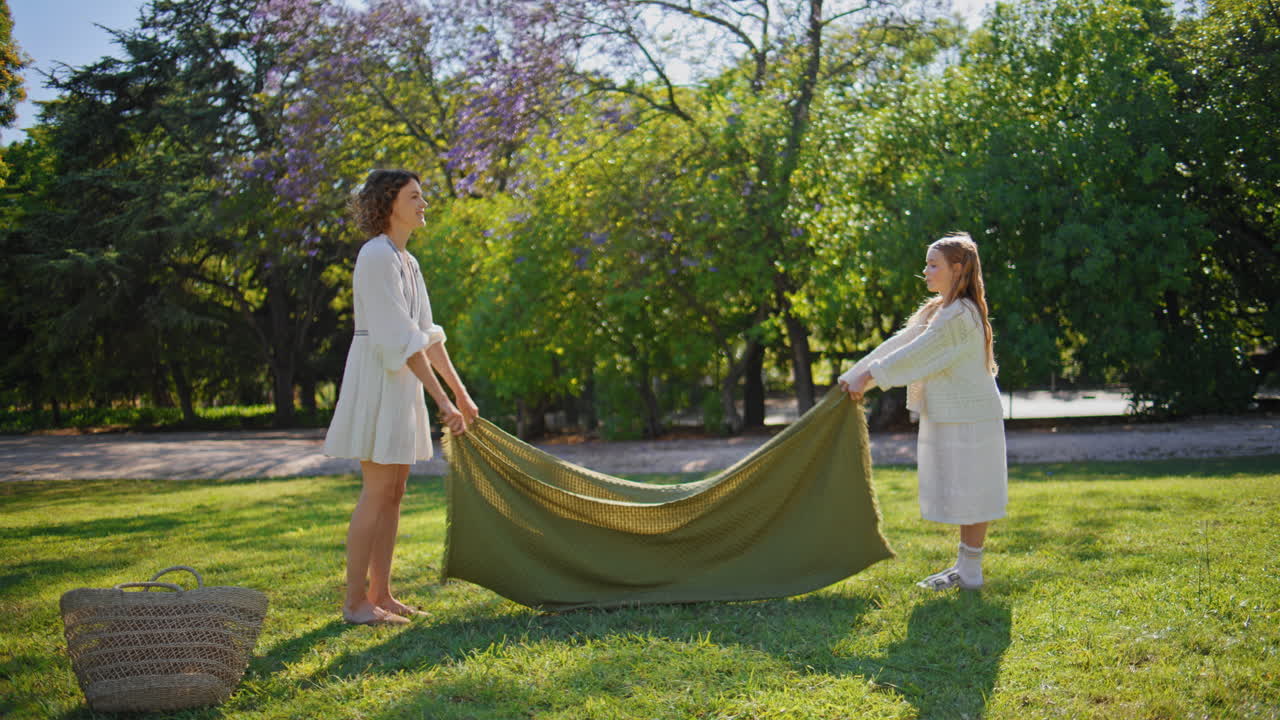 Little kid helping mother spread out blanket picnic. Family preparing for lunch