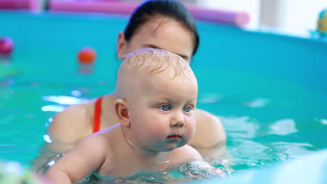woman is teaching a little baby boy to swim. happy child splashes his hands by the water and smiles. close up.