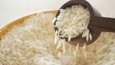 close up of uncooked white rice pouring from a wooden spoon into a bowl