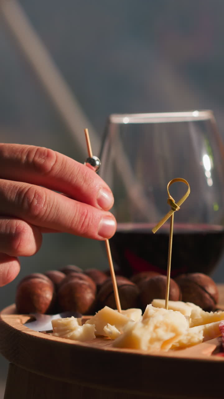 Male hand impales cheddar onto skewer closeup. Man enjoys assortment of delicious snacks at wine table in restaurant. Appetizers plate for romantic dinner