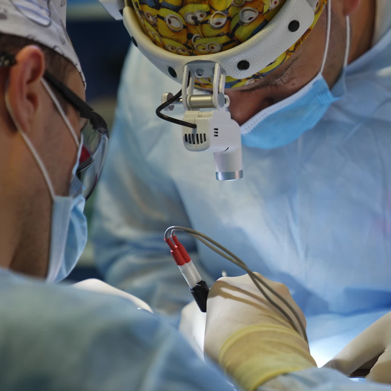 Operating surgeons bent low over the patient using tools. Doctors perform delicate work highlighting by the flashlights on their heads