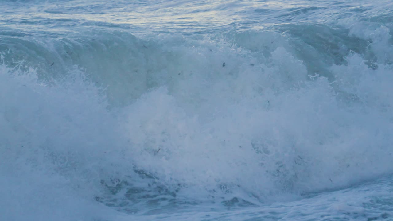 바다의 물결이 서서히 해변에 부히고 배경에는 물 위에 태양이 반사됩니다. - 영국 만 4k의 폭풍 상황에서 거친 바다 영상.