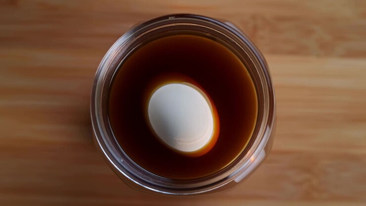 Close overhead view captures glossy liquid surface inside round glass container as reflection moves subtly, with warm illumination, wooden background texture, and centered minimal composition.