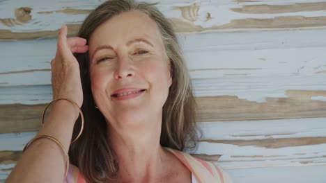 Portrait-of-happy-senior-caucasian-woman-laughing-by-weathered-blue-wooden-wall,-in-slow-motion