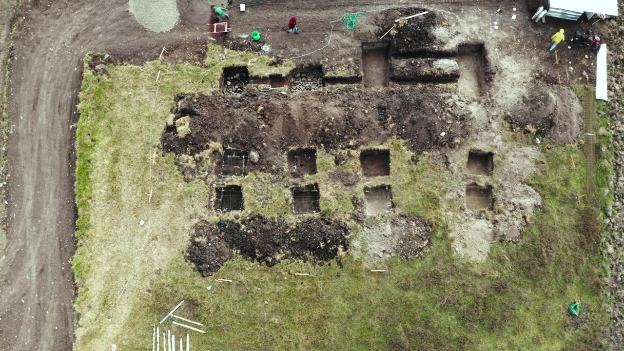The shot gradually descends, revealing in greater detail the trenches, pits, and temporary structures excavated in the surrounding terrain