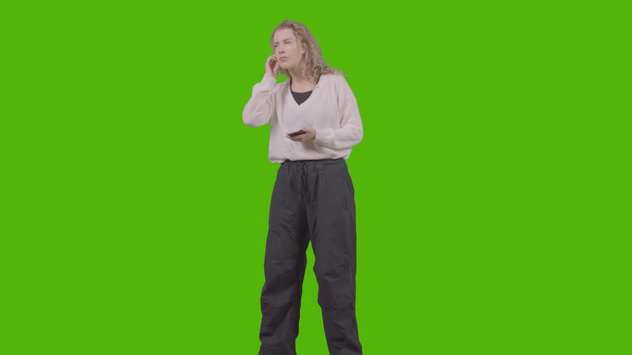 Scatto in studio a figura intera di giovane donna che ascolta musica sul telefono cellulare e balla su sfondo verde 2