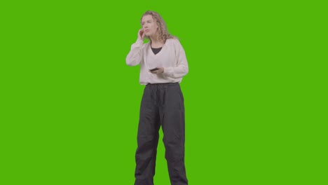 full length studio shot of young woman listening to music on mobile phone and dancing against green screen 2