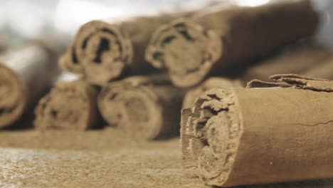 Cinnamom-stick-falling-on-table,-Pile-of-cinnamom-sticks-in-Background,-Slow-motion-shot