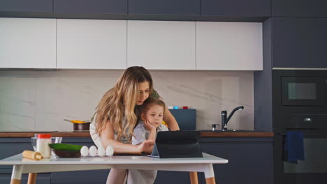 Mujer-Con-Hija-Busca-Recetas-Con-Tablet-En-La-Cocina