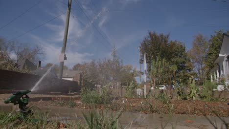 Slow-motion-shot-of-a-water-sprinkler-from-the-back-as-it-is-watering-a-lawn-during-the-day