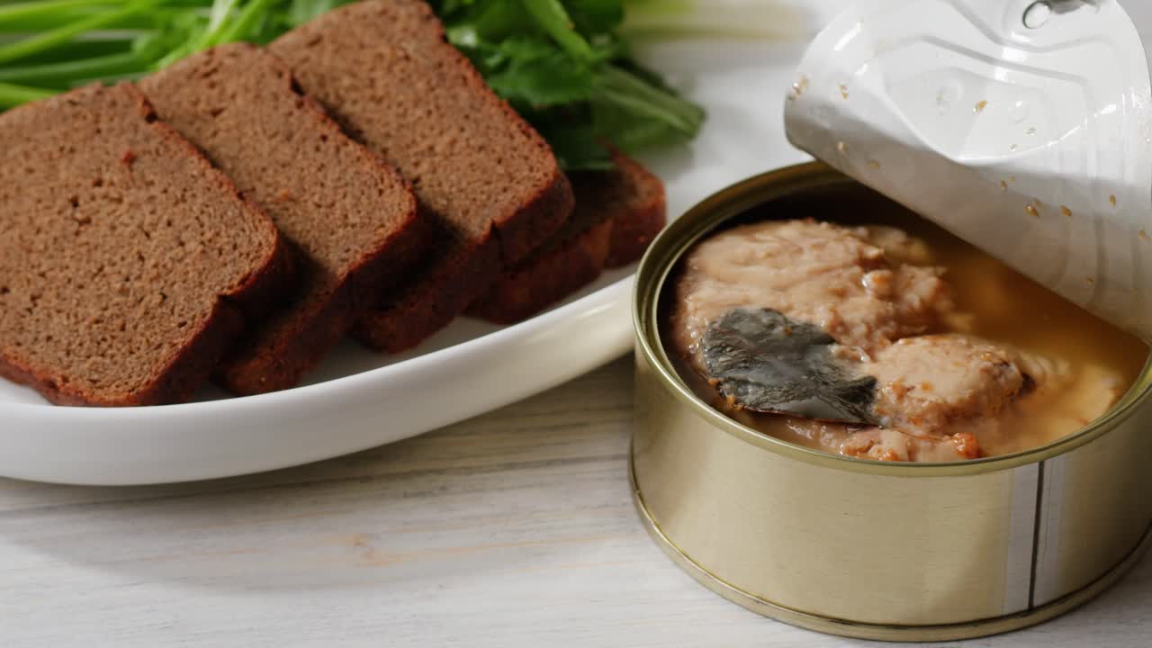 Smoked cod liver in oil in open tin can with fresh greens on wooden table. Seafoods delicacy. High quality 4k footage
