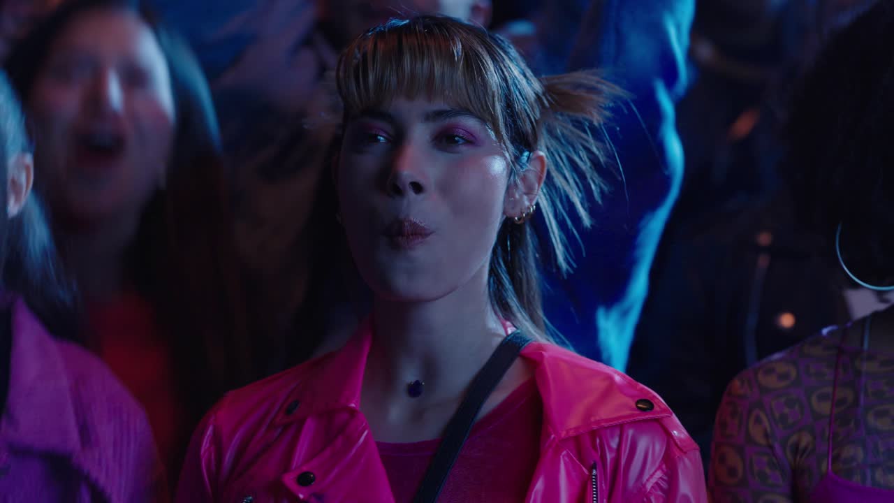 Beautiful girl watches a music concert at night with her friends while chewing gum