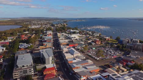 High aerial establishing of Belmont Wharf at sunset showing street lights, boats, and water fading to evening hue