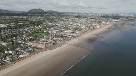 Portobello-beach-aerial-footage-showing-the-North-sea-at-low-tide,-buildings,-parks-and-Arthur's-Seat