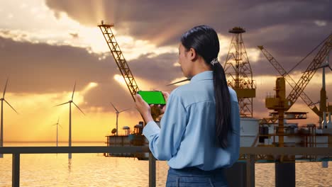 woman using smartphone at an oil rig with wind turbines