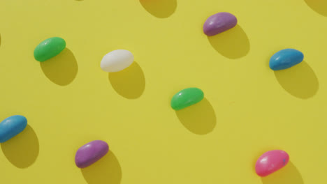 Video-of-overhead-view-of-rows-of-multi-coloured-sweets-over-yellow-background