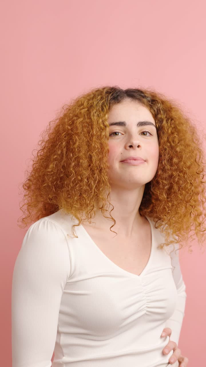 Young woman expressing disapproval with thumbs down on pink background