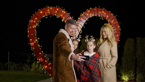 family taking selfie in front of heart-shaped lights