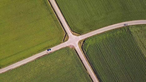 Bird-eye-view-of-a-perfect-symmetrical-crossroad-with-green-fields-and-2-cars-passing-by