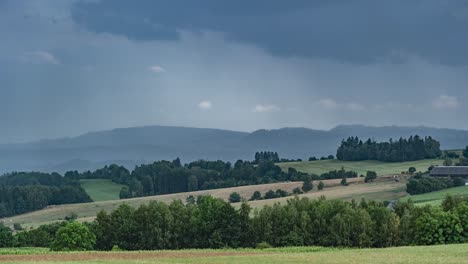 rainy clouds pass above the rural summer landscape of rolling hills, farm fields, and scattered forests