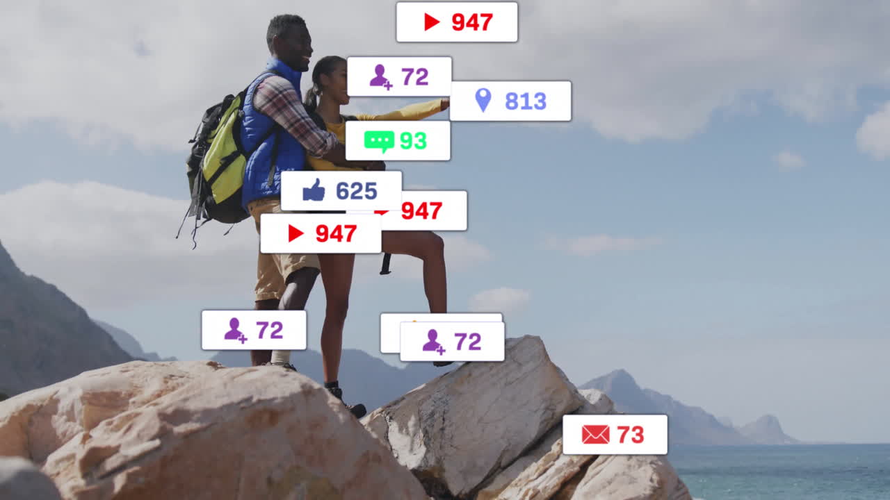 Hugging couple standing atop rocky seaside outcrop, showing floating social media reaction icons