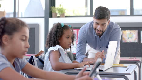 young asian man teaches in a school classroom with a laptop