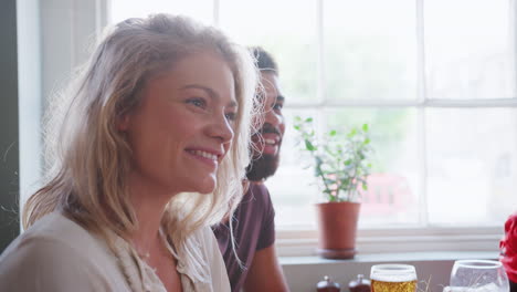 young adult man and woman sitting at a table in a pub listening to their friends talking, close up, selective focus