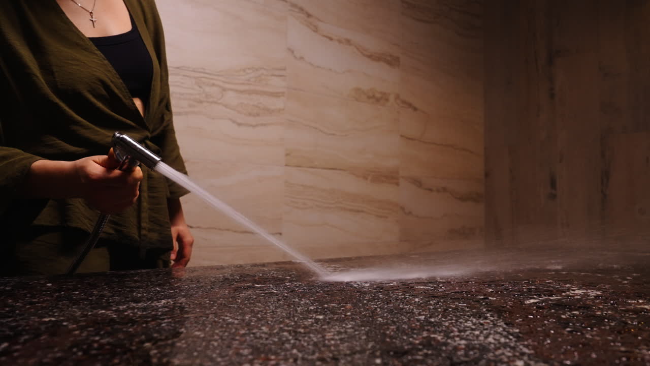 Woman Cleaning a Bathroom Countertop with a Spray Hose