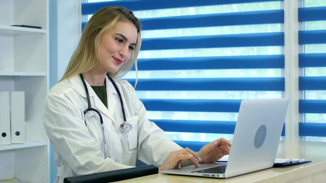 enfermera sonriente escribiendo en la computadora portátil y tomando notas en el escritorio de recepción