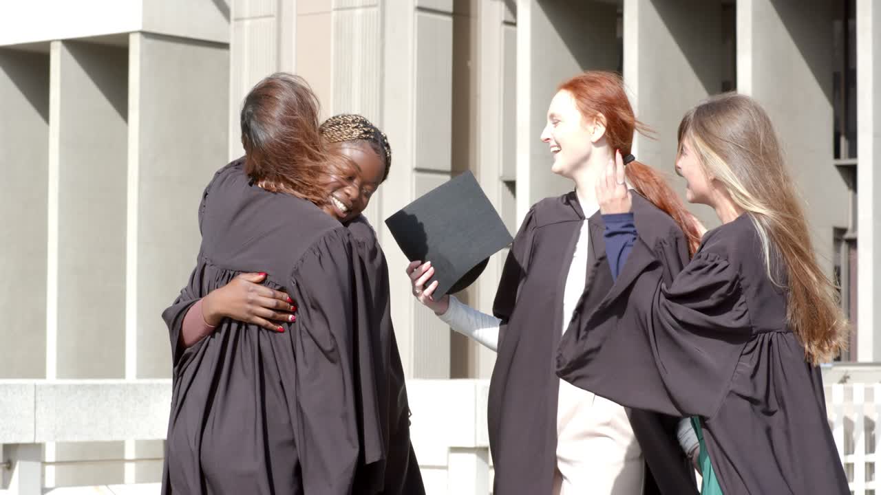 Amiche di diverse etnie che sollevano il tocco, lo lanciano, lo afferrano e festeggiano su una terrazza del campus.