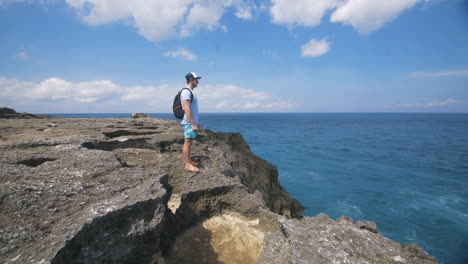 traveling man standing on edge of rocks looking out at ocean - pan up reveal