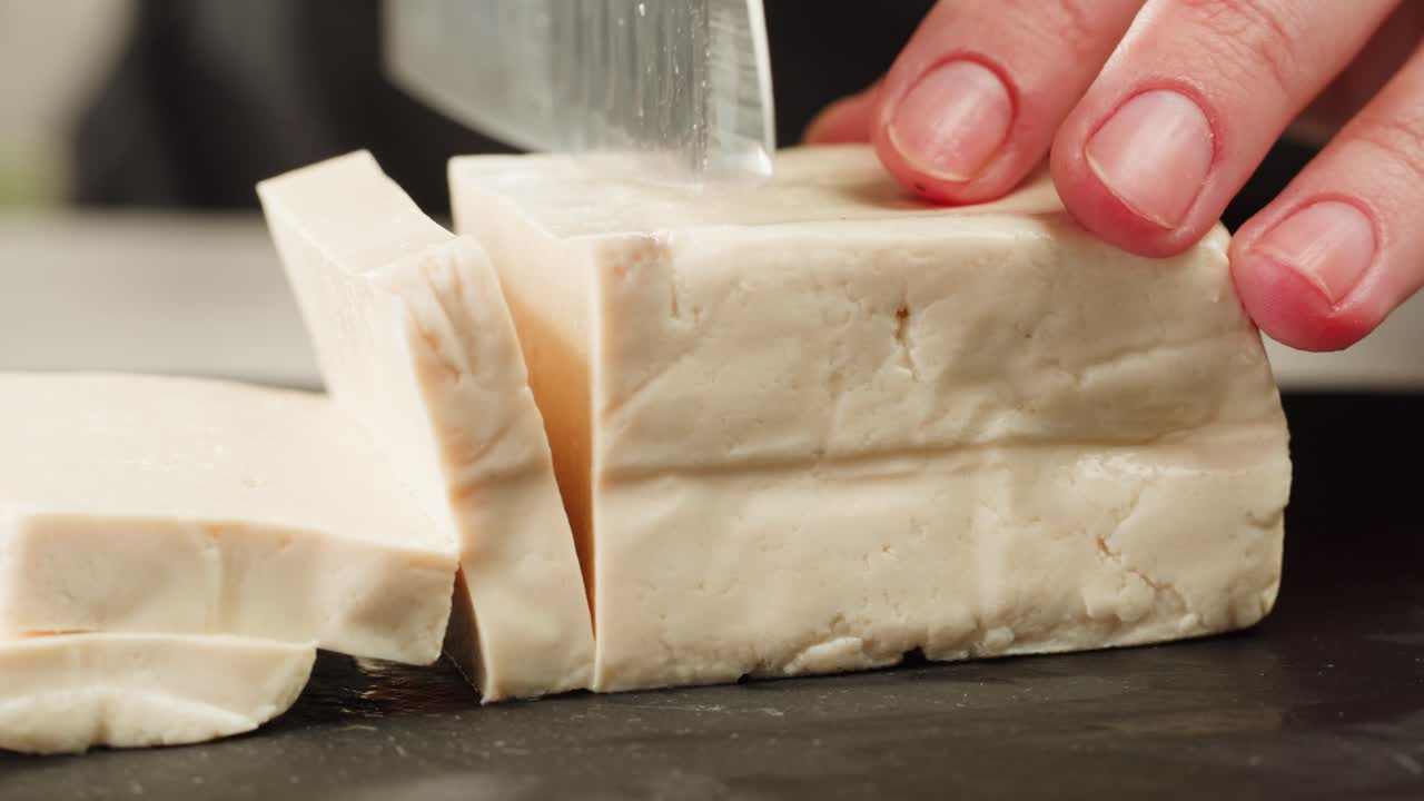 Fried tofu with sesame seeds and spices on cast iron pan, cooking japanese salad. Healthy ingredient for cooking vegan vegetarian diet food. Roasted tofu over black background.