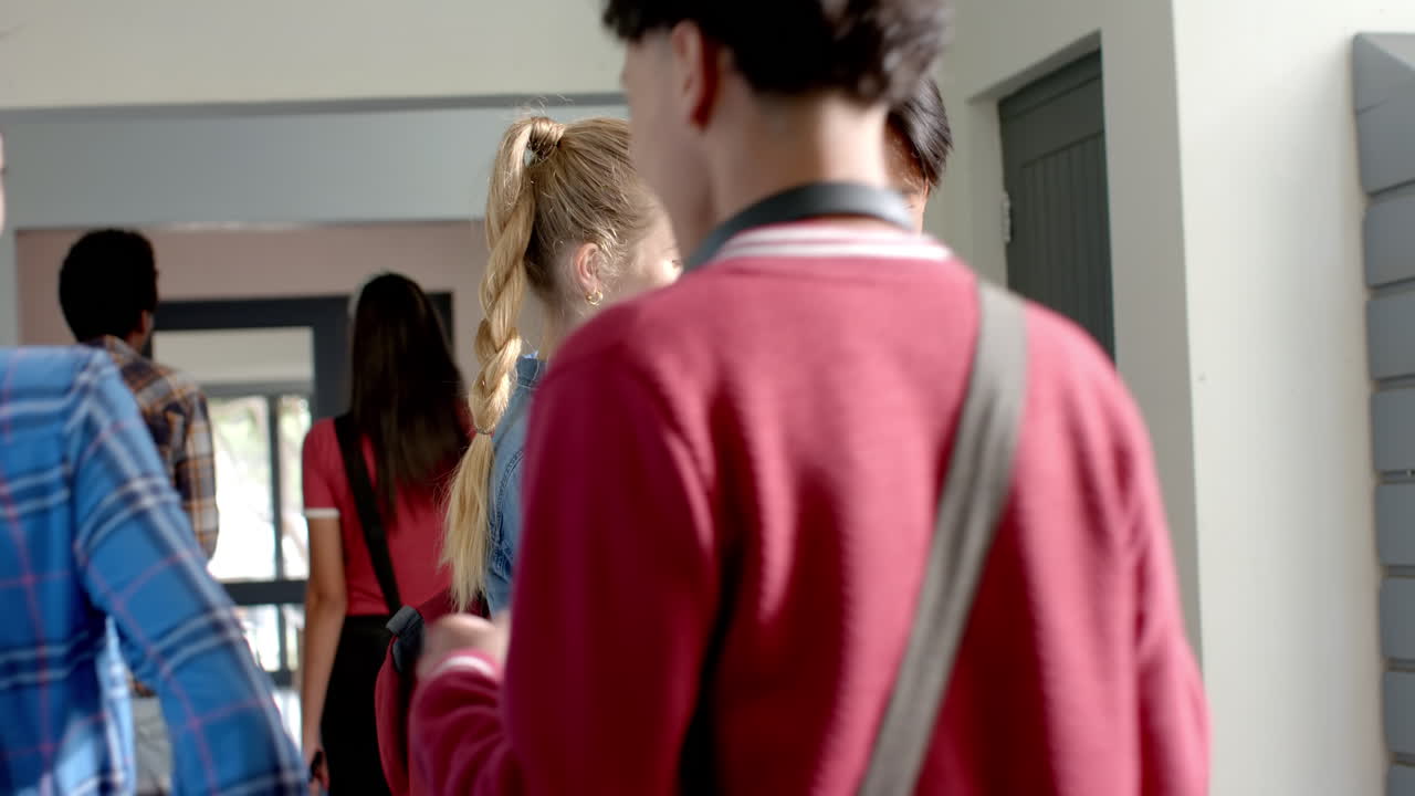 Walking in high school hallway, teenagers carrying backpacks and chatting