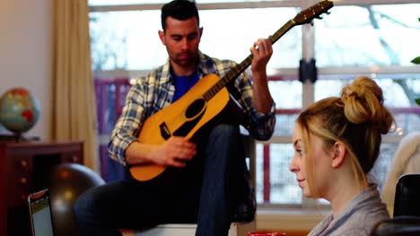 man playing guitar while woman using laptop