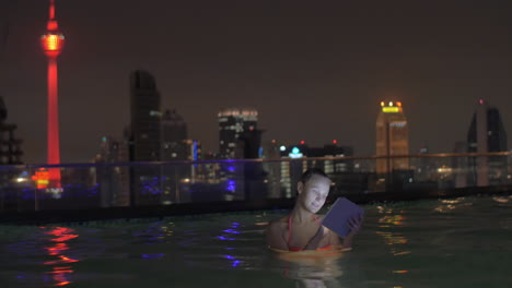 in pool on roof of a hotel in kuala lumpur malaysia is swimming young girl and works on tablet