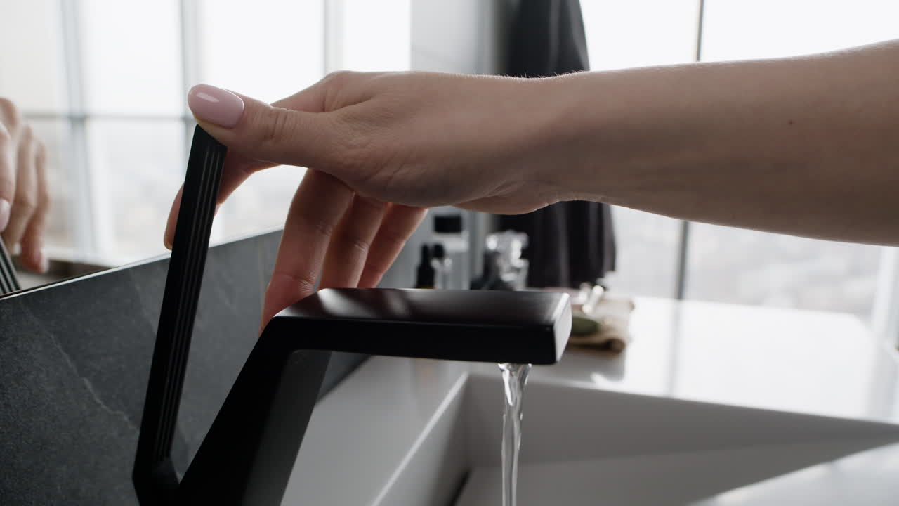Woman turning on a black modern bathroom faucet