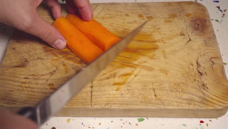 man slices carrot with knife on wooden cutting board, closeup on hands