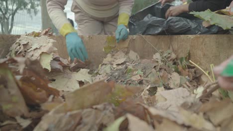women prepare a home wooden compost heap box. with their hands they remove the plastic from the natural elements.